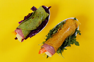 Flour tortilla wraps with ham, cheese and arugula on a yellow background.