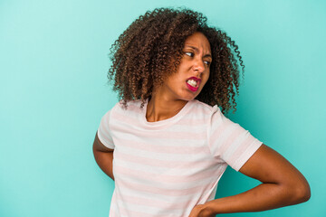 Young african american woman with curly hair isolated on blue background suffering a back pain.