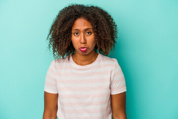 Young african american woman with curly hair isolated on blue background sad, serious face, feeling...