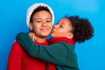 Photo of sweet charming dark skin kids dressed sweaters headwear scarf embracing kissing smiling...