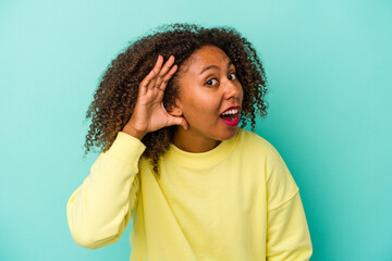 Fototapeta na wymiar Young african american woman with curly hair isolated on blue background trying to listening a gossip.