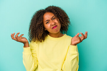 Young african american woman with curly hair isolated on blue background doubting and shrugging...