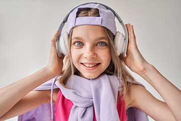 Girl standing and listening music with headphones at her head while looking at the camera