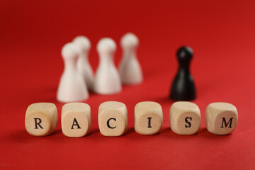 Word Racism made of wooden cubes with letters and black pawn among white ones on red background