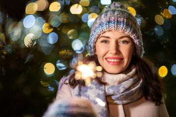 winter holidays, celebration and people concept - happy smiling woman with sparkler over christmas...
