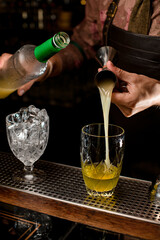hand of bartender skilfully pours drink from jigger into transparent glass