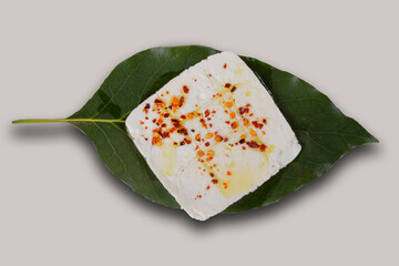 Roasted panela cheese with chile de arbol and olive oil on an avocado leaf with a green, pink, white, purple and yellow background.