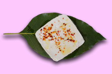 Roasted panela cheese with chile de arbol and olive oil on an avocado leaf with a green, pink, white, purple and yellow background.