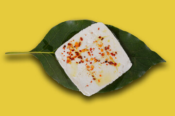 Roasted panela cheese with chile de arbol and olive oil on an avocado leaf with a green, pink, white, purple and yellow background.