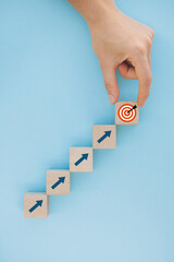 Close up of female hand arranging wood block stacking as step stair on blue background, putting...