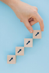 Close up of female hand arranging wood block stacking as step stair on blue background. Growth, success, strategy concept