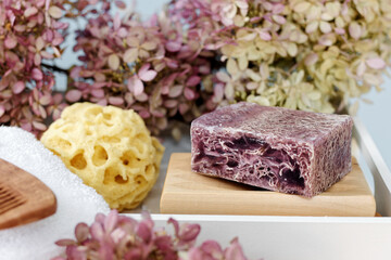 Purple soap with loofah with bio bath accessories among pink flowers. Romantic bath arrangement.
