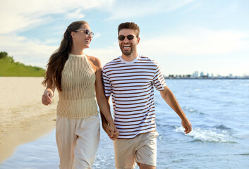 leisure, relationships and people concept - happy couple in sunglasses walking in water along summer beach