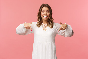 Portrait of enthusiastic upbeat young blond woman pointing fingers down to invite you check-out...