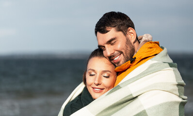 love, relationship and people concept - happy smiling couple in warm blanket on autumn beach