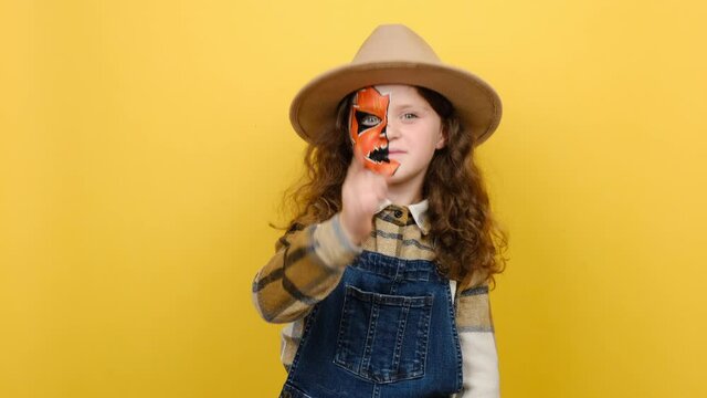Portrait of little girl kid with Halloween makeup mask wears hat and shirt, point index finger camera on you motivation encourage, isolated on yellow color background in studio. Party holiday concept
