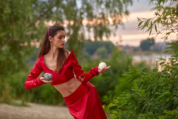 Ritual dance with candles in hands. Brunette woman in red costume for belly-dance is dancing on the beach