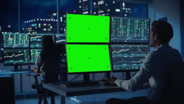 Financial Analyst Working on Computer with Multi-Monitor Workstation with Green Screen Chroma Key Mock Up Template and Real-Time Stock Charts. Businessman Works in Investment Bank Late in the Evening.