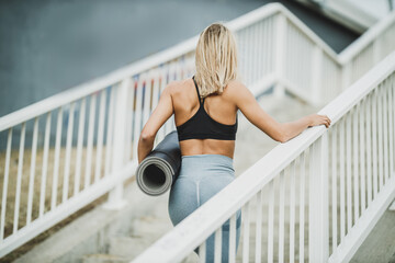 Woman Holding Rolled Up Yoga Mat And Walking Up The Stairs Before Training Outdoor