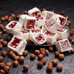 Pile of sweet Turkish Delight dessert with coconut and nuts served on plate on black table with scattered hazelnuts 