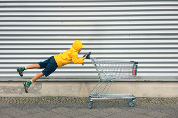 Girl with yellow jacket pushes shopping cart and flying gesture