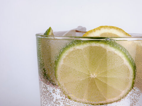Soda Water, Lime and Lemon Splashing Into Glass Of Water White Background