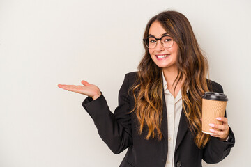 Young caucasian business woman holding a takeaway coffee isolated on white background showing a copy space on a palm and holding another hand on waist.