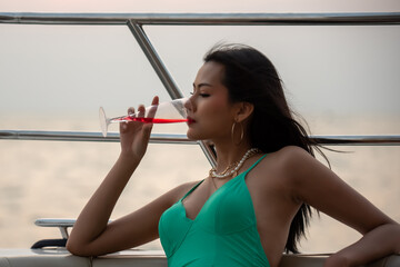 Young woman with drink in swimsuit posing on yacht in sunset