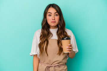 Naklejka premium Young caucasian store clerk woman holding a takeaway coffee isolated on blue background shrugs shoulders and open eyes confused.