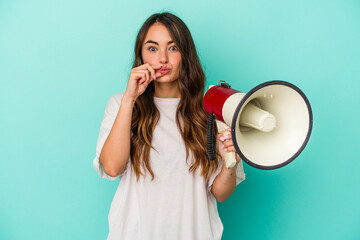 Young caucasian woman holding a megaphone isolated on blue background with fingers on lips keeping a secret.