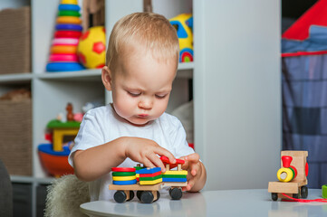 Handsome toddler plays with wooden toys in kindergarten or in children's room close-up and copy...