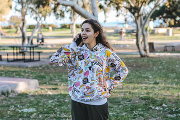 Cute young teenager girl talking with friends by phone. Pretty teen outside at the trees