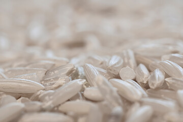 Fototapeta na wymiar Small grains of white rice. Macro photography in the kitchen. Chinese diet, raw uncooked food. Healthy eating. Selective focus on the texture of rice, blurred background.
