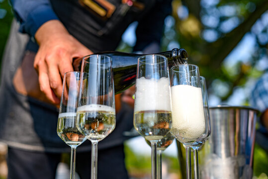 The Hand Of The Waiter Pouring Sparkling Wine Into The Glasses Outside