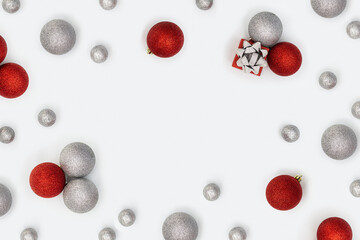 Christmas frame with sparkly red and silver Christmas balls and small gift box or present on white background. New Year holiday decorations  with copy space.