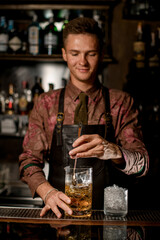 hand of man bartender holds long bar spoon and mixes cold drink into mixing cup