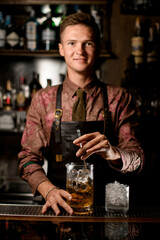 hand of male bartender holds long bar spoon and stirring cold drink into mixing cup