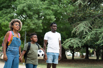 Black young family in a park after school. African American Mother and father spending time together with their happy and cute son outdoors in the nature. 