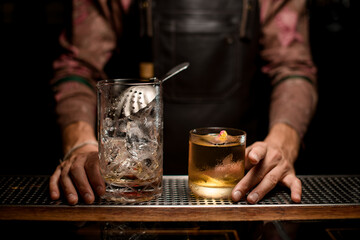 glassy mixing cup with ice and strainer on bar counter and glass with cocktail.
