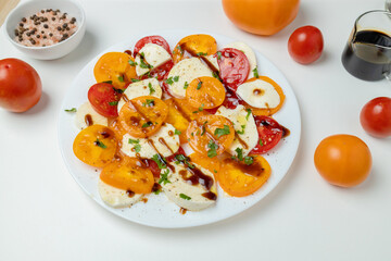 Fresh classic italian caprese salad with sliced red yellow tomatoes, mozzarella, olive oil, pepper and salt on light background. Healthy vegetarian diet food