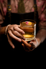 hands of man accurate holds glass of cocktail decorating with beautiful flower petal