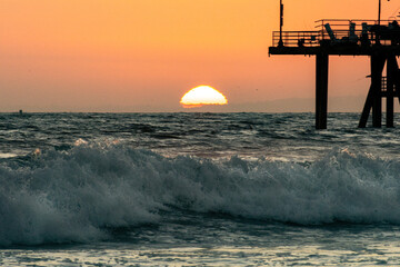 The sun sets into the waves of the Pacific Ocean off the coast of California by the famous landmark...