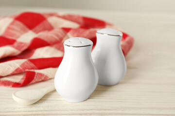 Ceramic salt and pepper shakers, spoon with napkin on white wooden table, closeup