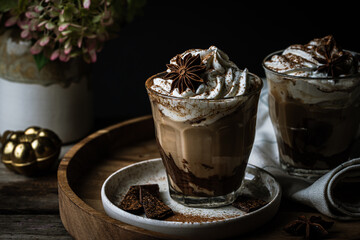 Two glasses of Pumpkin pie spice mocha latte with whipped cream and dark chocolate on plate on wooden tray on dark background .