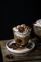 Two glasses of Pumpkin pie spice mocha latte with whipped cream and dark chocolate on plate on wooden table on dark background .