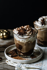 Two glasses of Pumpkin pie spice mocha latte with whipped cream and dark chocolate on plate on wooden table on dark background .