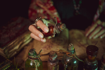 Female witch making potion on dark background, magic bottles with potions and candles on table of alchemist, Halloween theme
