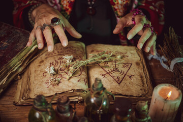Female witch making potion on dark background, magic bottles with potions and candles on table of...