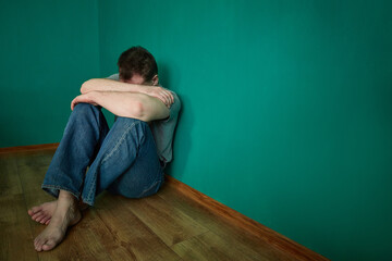 Man sits holding his head in a dark green depressing empty room.