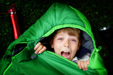 Preteen school kid boy in sleeping bag camping. Outdoors activity with children in summer. Fun and adventure camp, family and friends vacations or weekend trip. Portrait of child with flashlight.